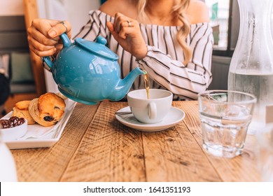 Cream tea, girl pouring tea from a teapot with scones