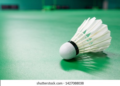 Cream white badminton shuttlecock and neon light shading on a green floor indoor badminton court , badminton sport wallpaper or background for presentation with copy space on the left 