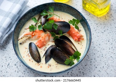Cream-soup with mussels and kamchatka crab served in a blue bowl on a light-grey granite background, horizontal shot