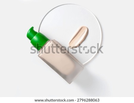A creamy beige sample of makeup base and a glass bottle on a white background