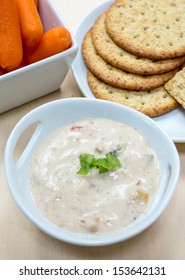 A creamy crab dip surrounded by vegetables and crackers at a party.