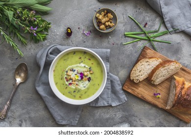 Creamy herbes soup with potatoes, herbes and sorrel, with edible blooms and croutons as topping. Gray concrete background. Top view. - Shutterstock ID 2004838592