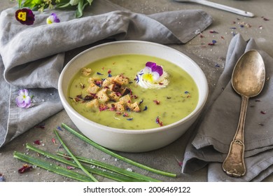 Creamy herbes soup with potatoes, herbes and sorrel, with edible blooms and croutons as topping. Gray concrete background. - Shutterstock ID 2006469122