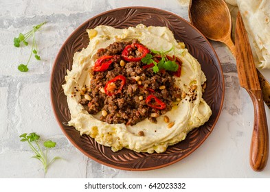 Creamy Hummus With Spicy Mutton Minced Meat In Clay Bowl On Stone Background. Ramadan Food. Top View