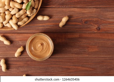 
creamy peanut butter in a glass jar and peanuts beans on wooden background top view