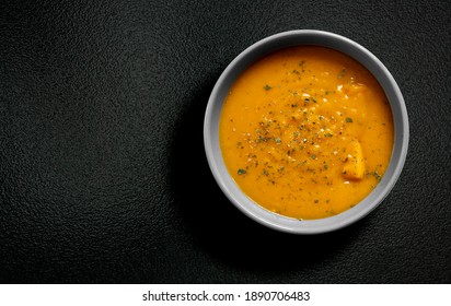 Creamy pumpkin soup  with chopped parsley and  thyme herb, cream and pumpkin with  pepper served in gray bowl on wooden black table background. top view