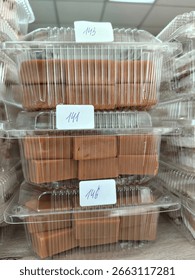 creamy rectangular candies in transparent plastic containers standing on top of each other on the counter in the store