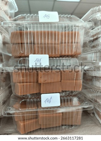 creamy rectangular candies in transparent plastic containers standing on top of each other on the counter in the store