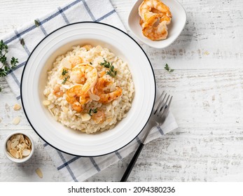 Creamy risotto with shrimps (fried prawns), parmesan cheese and thyme in white ceramic plate decorated with almond slices. Traditional medditerranean dish. Top view. Copy space. Black fork, napkin.