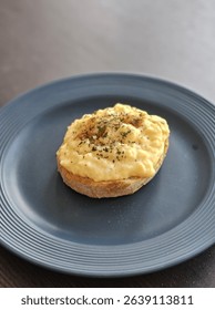Creamy scrambled eggs served on toasted sourdough bread, topped with cracked black pepper and herbs. Simple and delicious breakfast dish, plated on a dark ceramic plate in natural light.