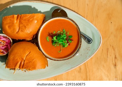 Creamy tomato soup garnished with microgreens, paired with toasted slider buns and pickled onions on an oval plate - Powered by Shutterstock