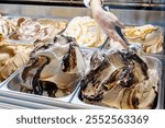 Creamy vanilla and chocolate ice cream being served with a scoop from a display case with multiple flavors in a dessert shop, food truck ice-cream stand. Ordering ice cream simple concept, one person