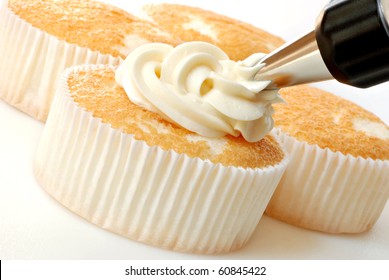 Creamy vanilla frosting being swirled onto individual sized angel food cakes with professional pastry tip.  Macro with shallow dof.