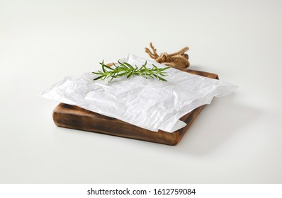 Creased Sheet Of White Wax Paper And Fresh Rosemary On Cutting Board