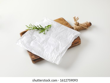 Creased sheet of white wax paper and fresh rosemary on cutting board