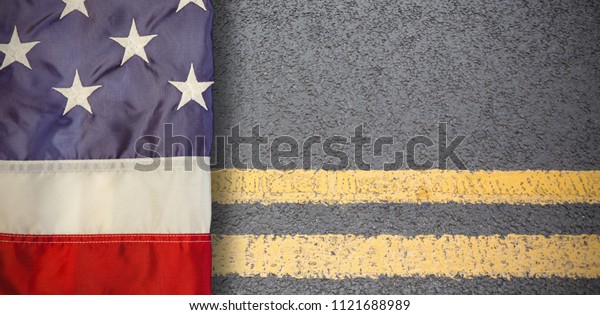 Creased US flag against yellow road marking on\
road surface