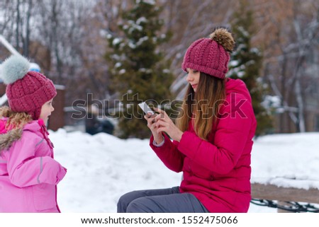 Create photo content using smartphone for family blog on social network. Stylishly dressed mother and daughter are photographed on a winter walk. Happiness to be a parent. Family look. Selfies.