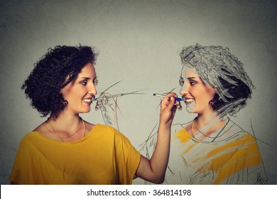 Create yourself, your image concept. Attractive young woman drawing a picture, sketch of herself isolated on grey wall background. Human face expressions, determination, creativity