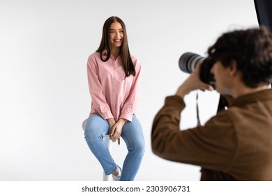 Creating captivating portraits. Photographer taking photos of young european lady in casual wear, having photoshoot on white background in modern studio
