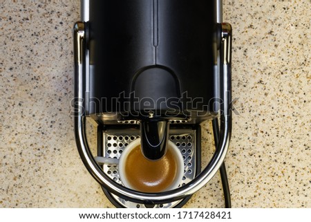 Creating espresso on an automatic machine using aluminum capsules. Kitchen bench with top view of coffeemaker with a white small cup on, used for making hot dripping coffee with rich cream.