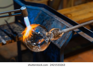 Creating glass art with hot torch and glassblowing pipe. The process of glass making.  Glassblower shaping the red melted glass. - Powered by Shutterstock