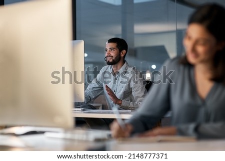 Creating happy customers is a 247 commitment. Shot of a young man using a headset and computer late at night in a modern office.