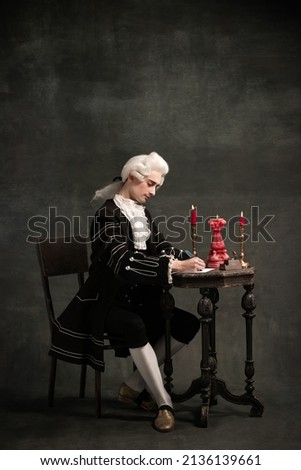 Creating music. Young man in image of Amadeus Mozart, medieval person isolated on dark vintage background. Retro style, comparison of eras concept. Elegant male model as historical character