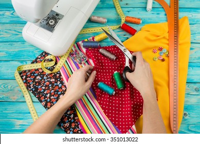 Creating A New Fashion. Sewing Process - Women's Hands Behind Her Sewing.  Sewing Machine With Many Sewing Utensils On Ablue Wooden Table. Top View. 