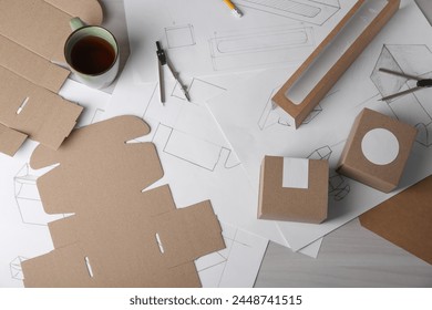 Creating packaging design. Drawings, boxes, coffee and stationery on light wooden table, flat lay