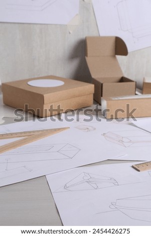 Creating packaging design. Drawings, boxes and ruler on light wooden table, closeup
