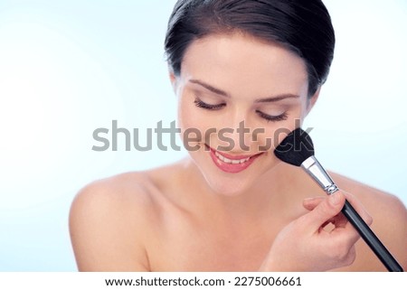Creating rosy cheeks. A young woman applying blush with a make-up brush.