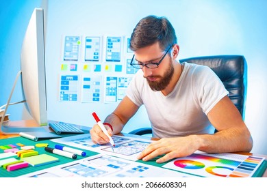 Creation of a mobile version of site. Man works in a studio to create websites. Mockups of mobile applications behind man back. Designer draws website interface on paper. Web designer at work - Shutterstock ID 2066608304