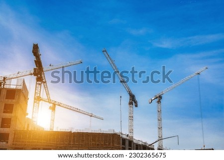 Creation site with industry cranes working at cloudy sky sunset backdrop. Bottom view of industrial crane on construction site. Concept of construction and renovation of buildings. Copy ad text space