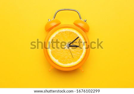 Creative alarm clock with citrus fruit on color background