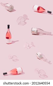 Creative angle pattern made of empty and full rose wine bottles and crystal glasses. Pastel pink background. Refreshing alcoholic summer drink concept.