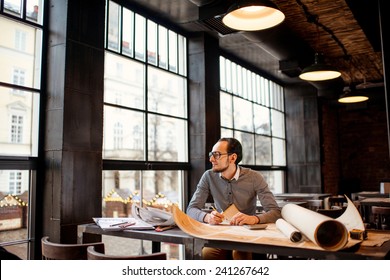 Creative architect thinking on the big drawings in the dark loft office or cafe. General plan with windows