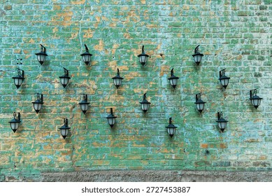 A creative architectural background featuring many vintage black outdoor lanterns arranged in a pattern on an old textured brick wall painted in fading green and yellow colors