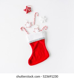 Creative Arrangement Of Bright Red Christmas Toys In Christmas Sock On White Background. Flat Lay, Top View