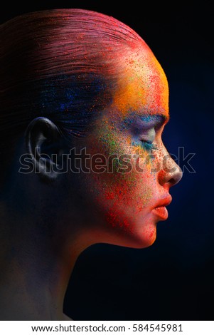 Creative art make up. Closeup cropped studio portrait of young fashion model with bright colorful mix of paint on her face. Color fantasy, artistic makeup. Side view or profile, vertical