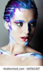 Creative art makeup of a young girl with blue eyes. Strokes of paint on his face and hair