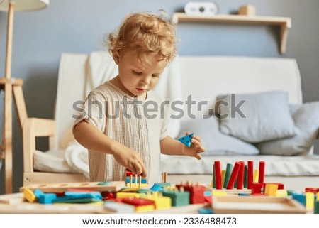 Creative art projects. Cognitive skill development. Montessori learning materials. Active playtime fun. Little blonde baby girl palying with wooden sorter toys at home interior.