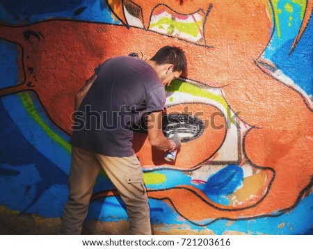 Creative art - teenage boy painting colorful abstract ornament graffiti on street wall with aerosol spray. Back view, overall plan