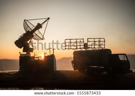 Creative artwork decoration. Silhouette of mobile air defence truck with radar antenna during sunset. Satellite dishes or radio antennas against evening sky. Selective focus