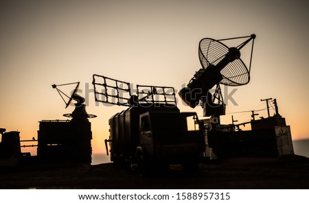 Creative artwork decoration. Silhouette of mobile air defence truck with radar antenna during sunset. Satellite dishes or radio antennas against evening sky. Selective focus