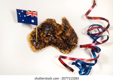Creative Australia Day breakfast toast with vegemite cutout in the shape of Australia with a small flag and blue and red ribbons isolated on a white background.
