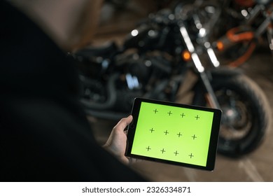 Creative authentic motorcycle workshop Biker mechanic in garage standing near motorcycle holding green screen tablet - Powered by Shutterstock