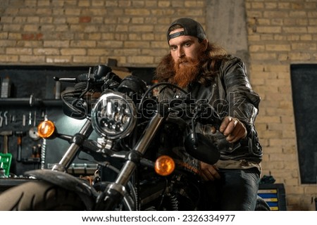 Creative authentic motorcycle workshop garage portrait serious redhead bearded biker mechanic sitting motorcycle