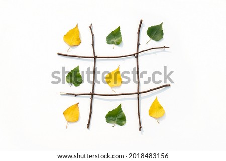 Creative autumn concept. Tic-tac-toe, noughts and crosses between summer and autumn. Green and yellow leaves in grid made from branches. Fall is the winner. Top view Flat lay. Stock photo © 