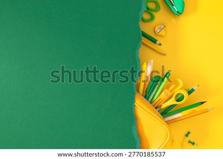 Creative back to school background with green torn paper and yellow stationery supplies including pencil case, scissors, and pencils on yellow surface. Flat lay with large copy space for text.