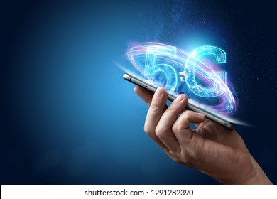 Creative background, male hand holding a phone with a 5G hologram on the background of the city. The concept of 5G network, high-speed mobile Internet, new generation networks. Mixed media. - Shutterstock ID 1291282390